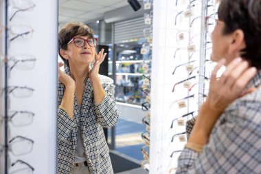 Optical store. Mid aged good-looking lady trying on eyeglasses at the optical store