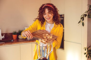 Making smoothie. Young girl putting slices of banana to the shaker