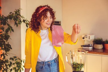 Making smoothie. Happy young girl making smoothie and looking contented