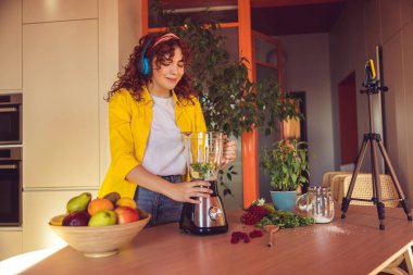 In the kitchen. Curly-haired girl looking involved while making smoothie in the kitchen
