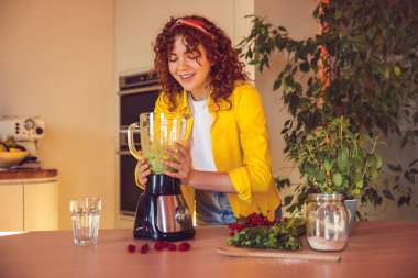 In the kitchen. Curly-haired girl looking involved while making smoothie in the kitchen