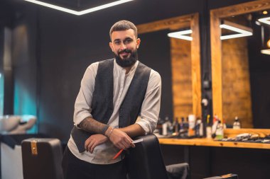 Stylish barber. Dark-haired bearded man in a stylish outfit looking confident