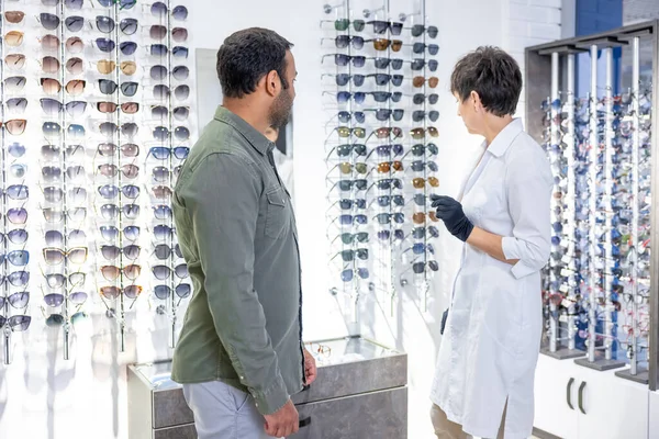 Optical store. Female optometrist helping a visitor to buy new eyeglasses
