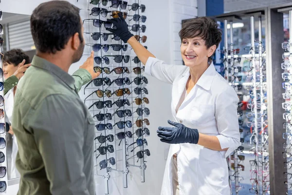 Optical store. Female optometrist helping a visitor to buy new eyeglasses