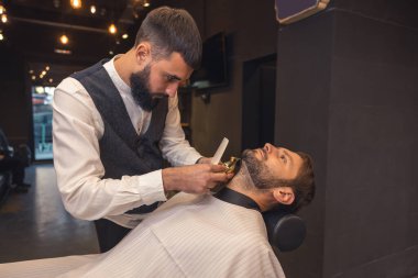 Barber service. Professional barber carefully trimming the clients beard