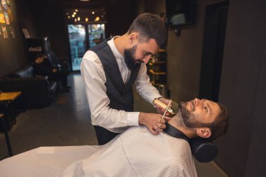 Barber service. Professional barber carefully trimming the clients beard