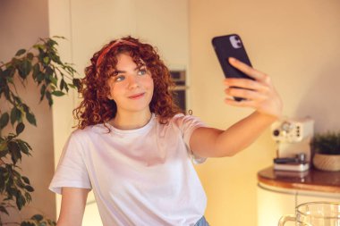 Selfie. Curly-haired young girl making selfie in the kitchen