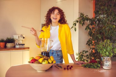 Making smoothie. Young cute girl in yellow jacket making smoothie in the kitchen