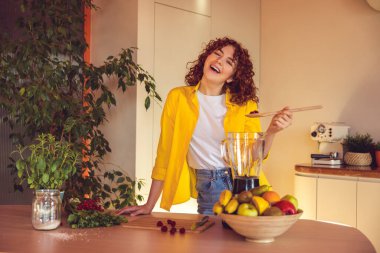 Making smoothie. Young cute girl in yellow jacket making smoothie in the kitchen