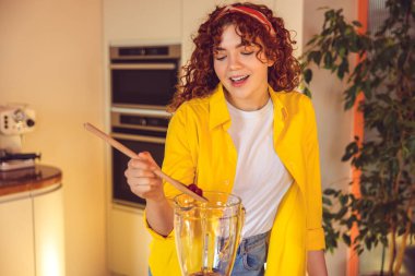Making smoothie. Young cute girl in yellow jacket making smoothie in the kitchen