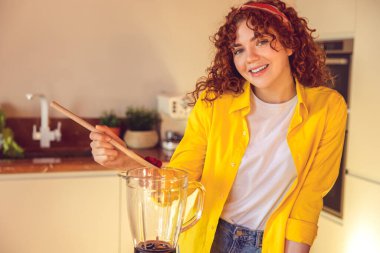 Making smoothie. Young cute girl in yellow jacket making smoothie in the kitchen
