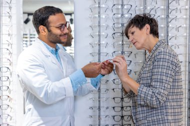 Optical store. Male optometrist helping a woman to choose eyeglasses