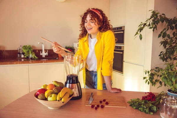 Making smoothie. Young cute girl in yellow jacket making smoothie in the kitchen