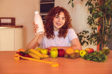 Breakfast time. Smiling curly-haired girl sitting at the table with a bottle of milk in hand