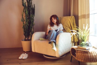 Making notes. Cute girl in headphones sitting in the armchair with diary in hands