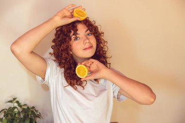 Love citrus. Curly-haired ginger girl with slices of orange in hands