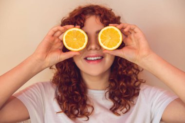 Love citrus. Curly-haired ginger girl with slices of orange in hands