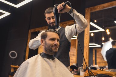Barbershop. Barber drying clients hair and looking concentrated