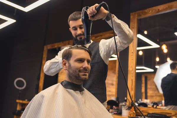 Barbershop. Barber drying clients hair and looking concentrated