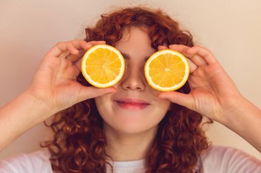 Love citrus. Curly-haired ginger girl with slices of orange in hands