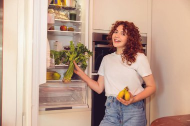 In the kitchen. Ginger girl unpacking and putting food to the fridge