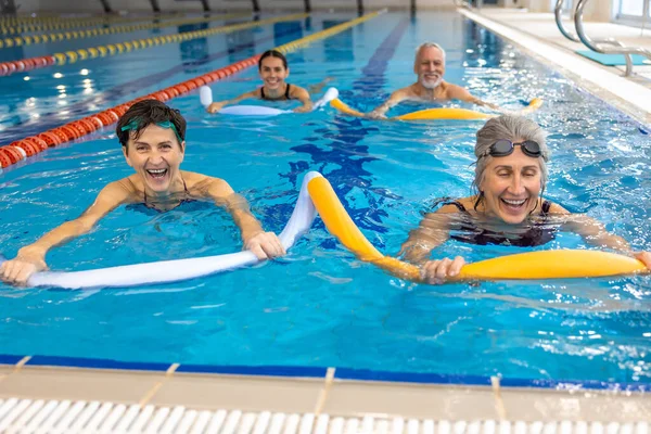 Water fitness class. Group of people working with float noodles at water fitness class