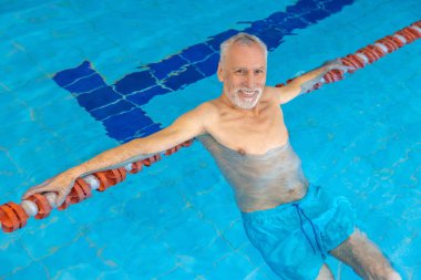Male swimmer. Gray-haired bearded swimmer looking contented at the swimming pool