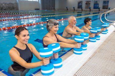Exercise with dumbbells. Group of seniors having an exercise with dumbbels during water aerobics class