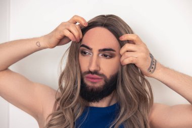 Portrait of a sad pensive bearded young man putting on the wig over the head