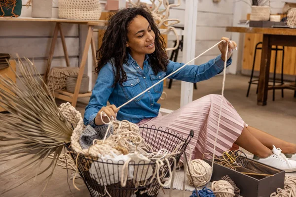 Mactame tools. Young woman sitting on the floor and looking at macrame tools