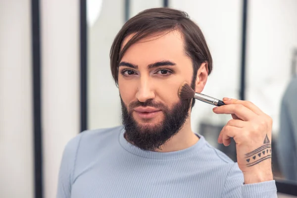 Headshot of a cute young man applying powder to the cheek with a makeup brush