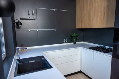 Minimalist tarzda dekore edilmiş beyaz dolapları ve siyah duvarları olan samimi modern mutfak.