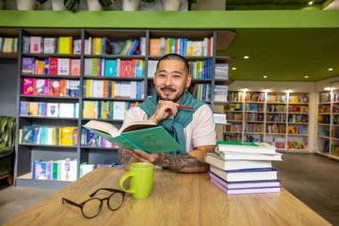 Kütüphanede. Genç Asyalı bir adam elinde kitapla kütüphanede oturuyor.