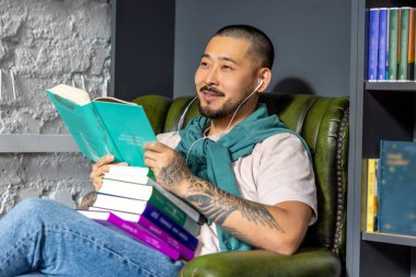 Kütüphanede. Genç Asyalı bir adam elinde kitapla kütüphanede oturuyor.