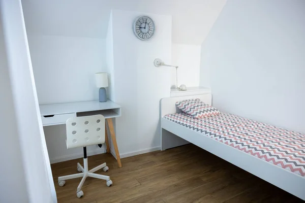 Attic room with a writing desk and the comfortable bed placed against the white wall