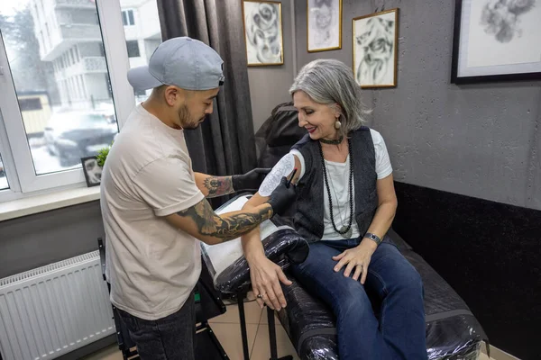 in the tattoo salon. Grey-haired woman getting ready for tattoo session