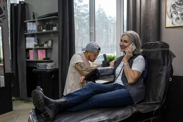 Salão Tatuagens Mulher Cabelos Grisalhos Falando Telefone Enquanto Mestre Tatuagem — Fotografia de Stock