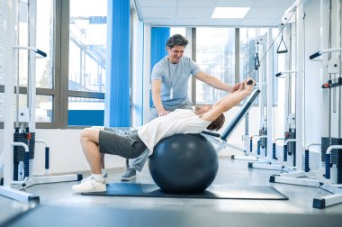 Rehabilitasyon egzersizleri. Erkek hasta bir spor salonunda rehabilitasyon egzersizi yapıyor.