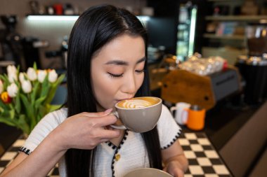 Kafedeki seramik bardaktan köpükle cappuccino yudumlayan sakin bir esmer portresi