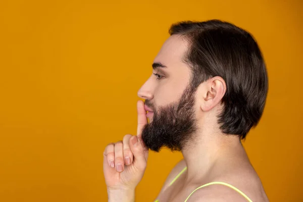 大胡子变性人手指头靠近嘴唇做沉默手势的侧面肖像在橙色背景上保持隐蔽姿势隔离 — 图库照片
