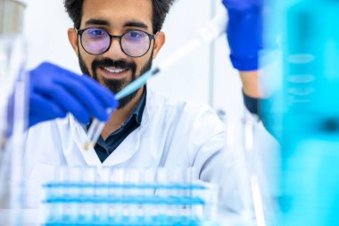 Koruyucu eldivenler giyen bilim adamı tüpleri test etmek için kimyasallar damlatıyor, biyokimyacı yeni ilaçlar keşfetmek için deneyler yapıyor, bilim laboratuvarında çalışıyor..