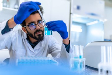 Gözlüklü ve cerrahi eldivenli sakallı bilim adamı laboratuarda cam, bilim ya da kimya araştırma ve geliştirme ile kimyasal numuneyi test ediyor..