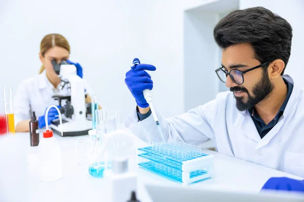 在现代实验室 科学家小组检查样品 女医生使用显微镜 男性研究人员在烧瓶中处理化学液体 — 图库照片