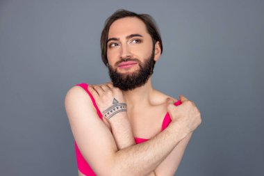 Düşünceli esmer transseksüel pembe bluz giyiyor, kendine sarılıyor. Gri arka planda izole edilmiş bir gelecek hayali kuruyor.