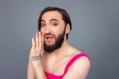 İyimser, neşeli, transseksüel, pembe bluz giyen transseksüel el ele tutuşup gri arka planda izole edilmiş bir sırrı paylaşıyor.