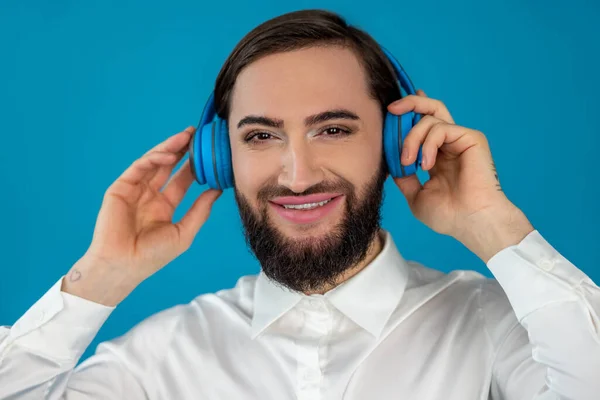 幸せな陽気なトランスジェンダーの男リッスン彼のお気に入りの曲のヘッドフォンでカメラを見ますとともに笑顔と楽しい顔隔離された上の青の背景 — ストック写真