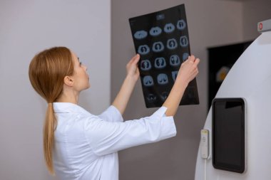 Genç sarışın kadın doktor MRI makinesinin yanında duran klinikte MRI fotoğrafını kontrol ediyor..