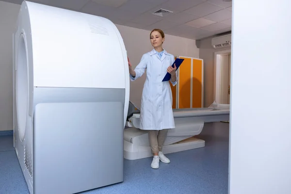 stock image Female doctor professional in magnetic resonance imaging or computed tomography room of a modern hospital, making notes of diagnostics.