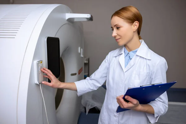 利用控制面板在现代诊断学的磁共振成像或计算机断层扫描室中穿着实验室外套的女医生 — 图库照片