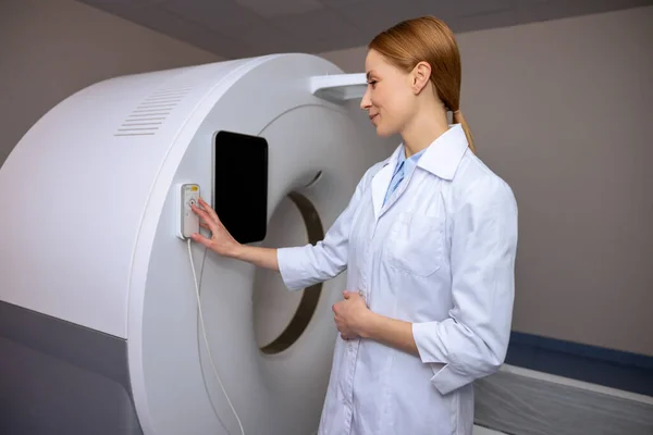 磁気共鳴画像法又は現代診療所製造診断法の計算断層撮影室に研究室のコートを着ている女性医師 コントロールパネルを使用して — ストック写真